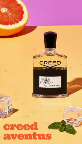Creed Aventus perfume bottle with an orange, ice cubes, and mint leaves on a yellow and purple background.