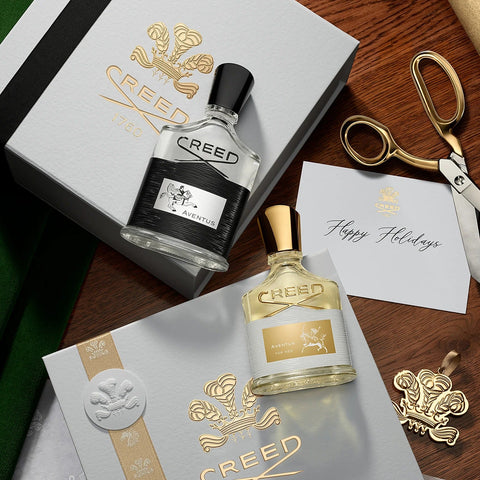 Two bottles of Creed perfume with packaging and a card on a wooden surface.